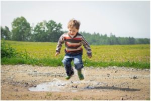 little kid jumping in puddle of water in a field